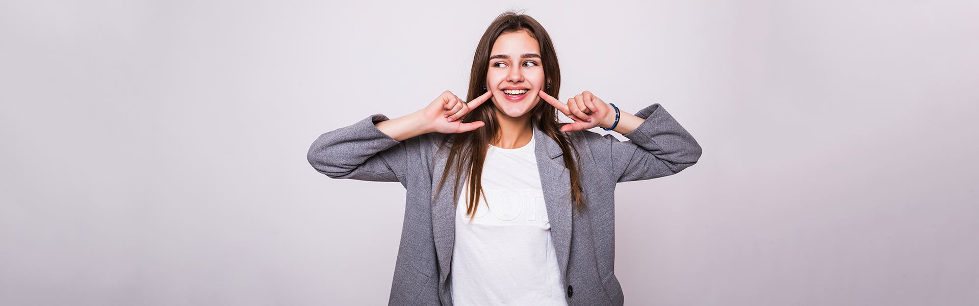 Smiling woman pointing at her teeth after dental crown treatment in Cambridge