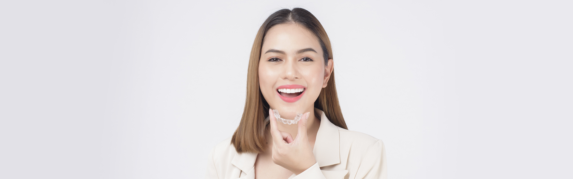 Smiling woman holding Invisalign aligner in Cambridge dental clinic