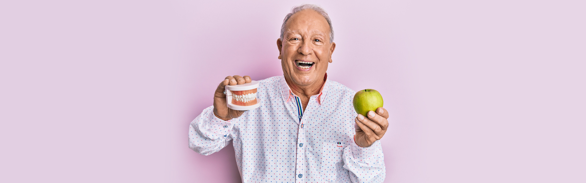 Senior man holding dentures and apple after dental care in Cambridge